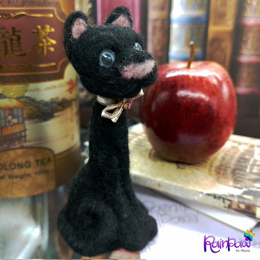 Felted black cat with a red apple and tea package in the background