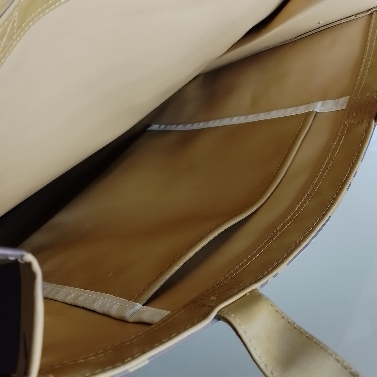 Close-up of the beige interior lining of a tote bag, showing stitched compartments and a strap attachment.