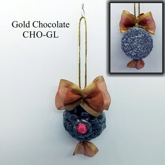 A decorative ornament made to resemble a pine cone; the air-hardening clay is painted in brown and gold acrylic paint with a shiny pink gem at its centre and silver slitter on the base. The golden pine cone is adorned with a large brown and gold ribbon. Suspended by its thin gold string, it gives off an elegant and festive appearance.