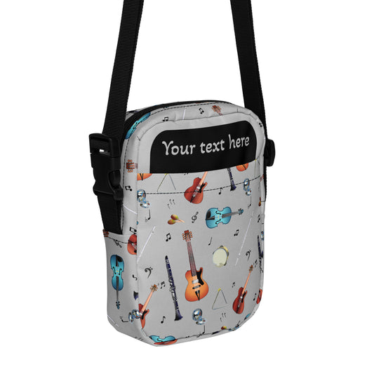 Grey crossbody bag with black adjustable shoulder strap (with black plastic clip), inside and outside pockets, sturdy fabric, and two-way zipper. The design features a repeat pattern of colourful musical instruments and black musical notes on a grey background.
