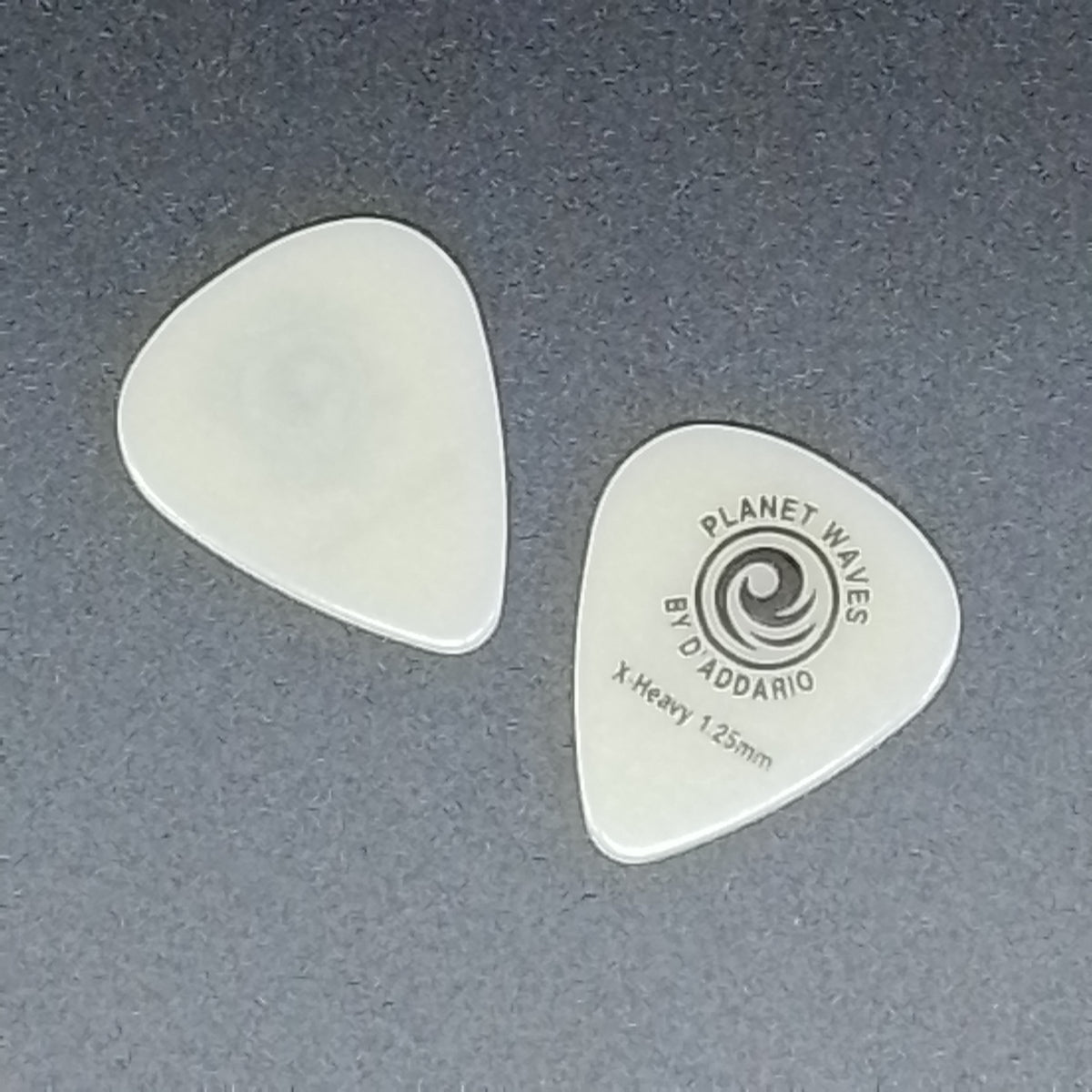 Two plastic guitar picks on a dark grey textured background, with one pick showing the Planet Waves by D'Addario branding.