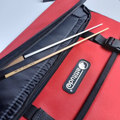 A close-up of a red and black Attitude brand bag with a black zipper, showing two wooden batons resting inside.