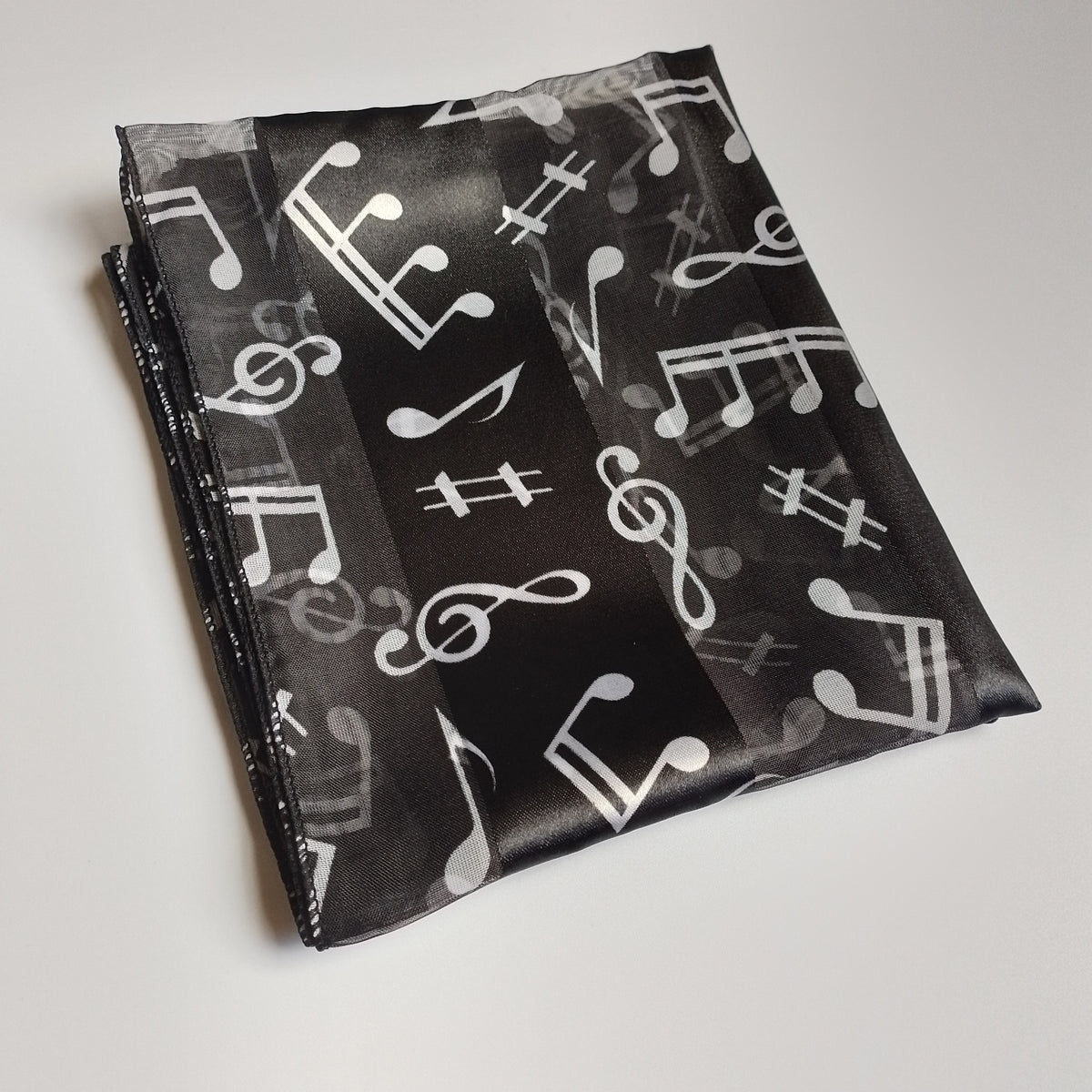 A folded black fabric accessory, a scarf featuring a white and white musical note pattern, displayed on a white background.
