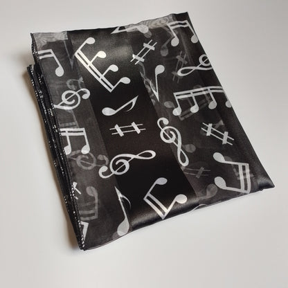 A folded black fabric accessory, a scarf featuring a white and white musical note pattern, displayed on a white background.