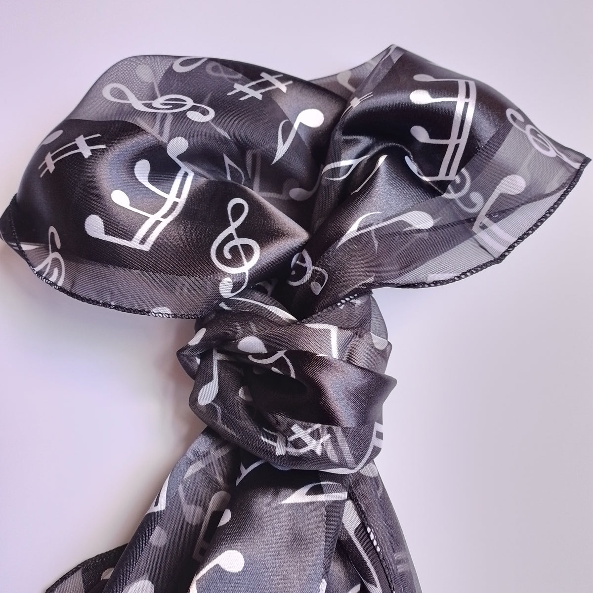 A sheer black scarf with a white music note and staff pattern, tied in a loose knot against a light background.