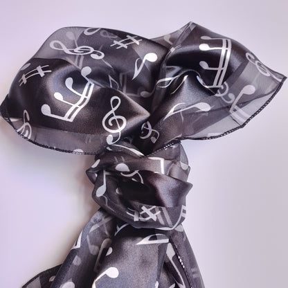 A sheer black scarf with a white music note and staff pattern, tied in a loose knot against a light background.