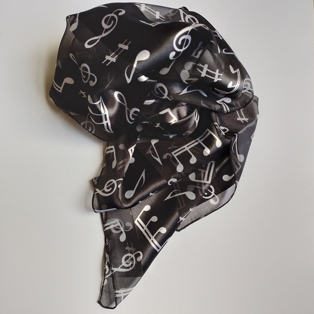 A lightweight black scarf with a white musical note pattern, styled in a loose knot on a plain white surface.