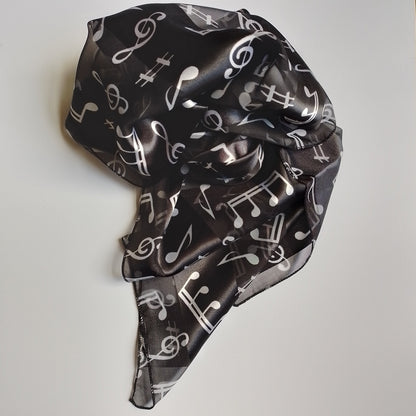 A lightweight black scarf with a white musical note pattern, styled in a loose knot on a plain white surface.