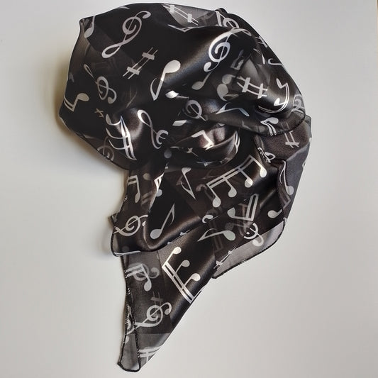 A lightweight black scarf with a white musical note pattern, styled in a loose knot on a plain white surface.