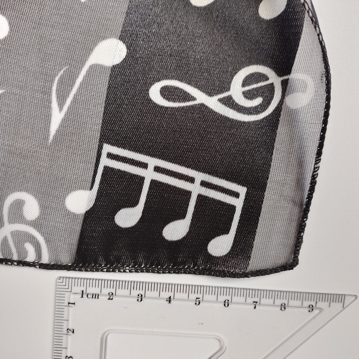 Black and white sheer mesh fabric with a white musical note pattern, shown with a clear plastic ruler for scale.