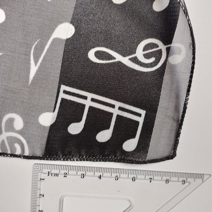 Black and white sheer mesh fabric with a white musical note pattern, shown with a clear plastic ruler for scale.
