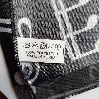 Close-up of a black and white patterned scarf with a white sewn-in care label reading '100% POLYESTER MADE IN KOREA'.