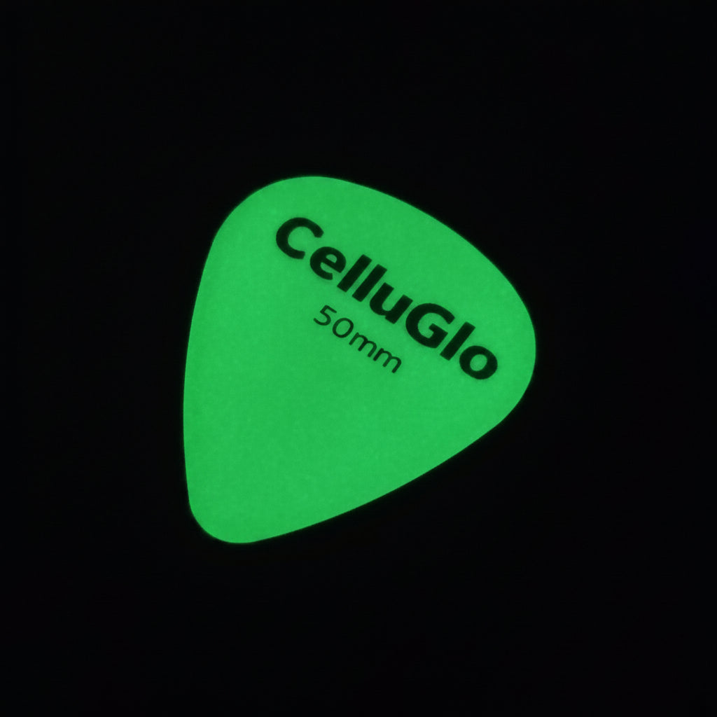 A green CelluGlo glow-in-the-dark guitar pick on a black background.