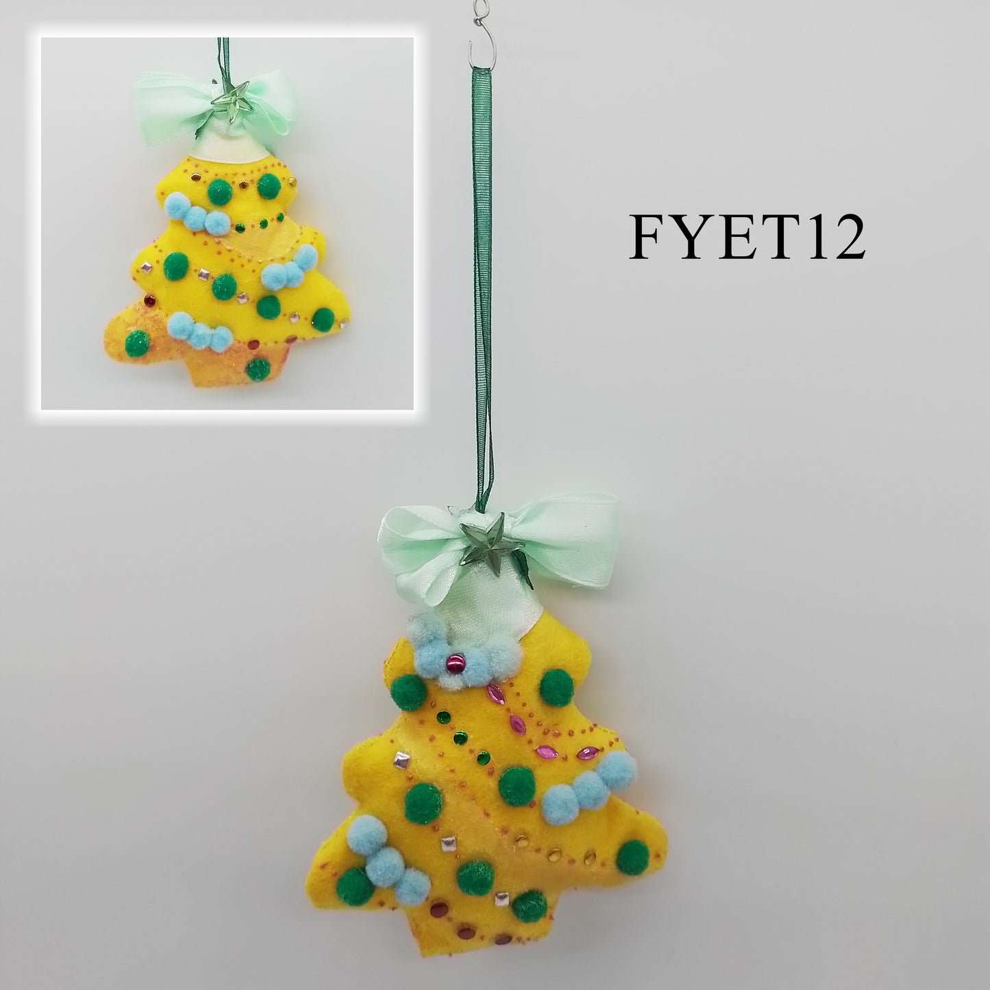 A yellow felt ornament shaped like a Christmas tree, decorated with green and light blue pom-poms, coloured studs, a light green ribbon and two star-shaped rhinestones. The tree features a glittery texture on its edges, adding a festive touch.
A green, thin ribbon is attached to one end to form the hanger.