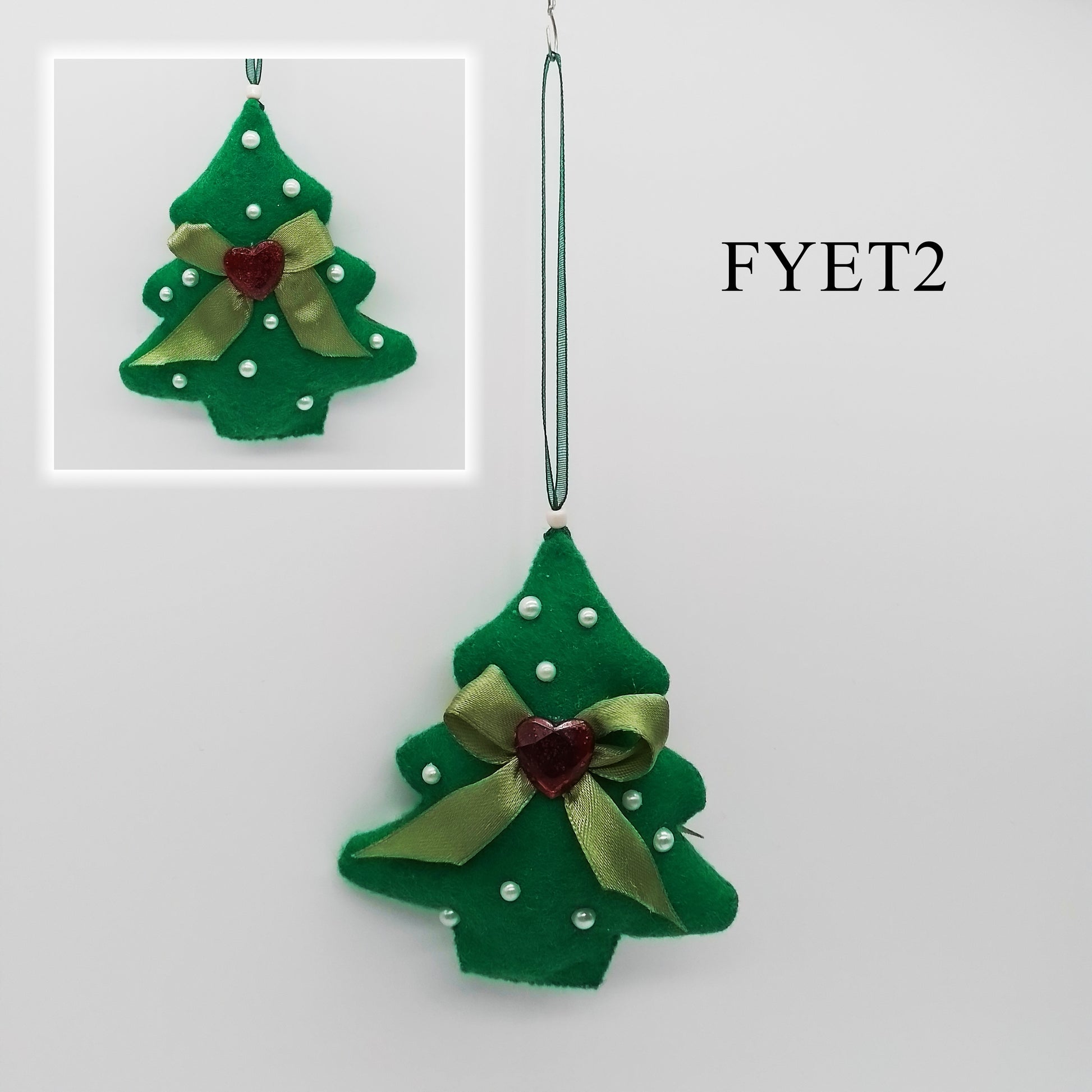 The felt tree is adorned with small white beads and features a decorative green bow with a red heart at its centre on either side.
