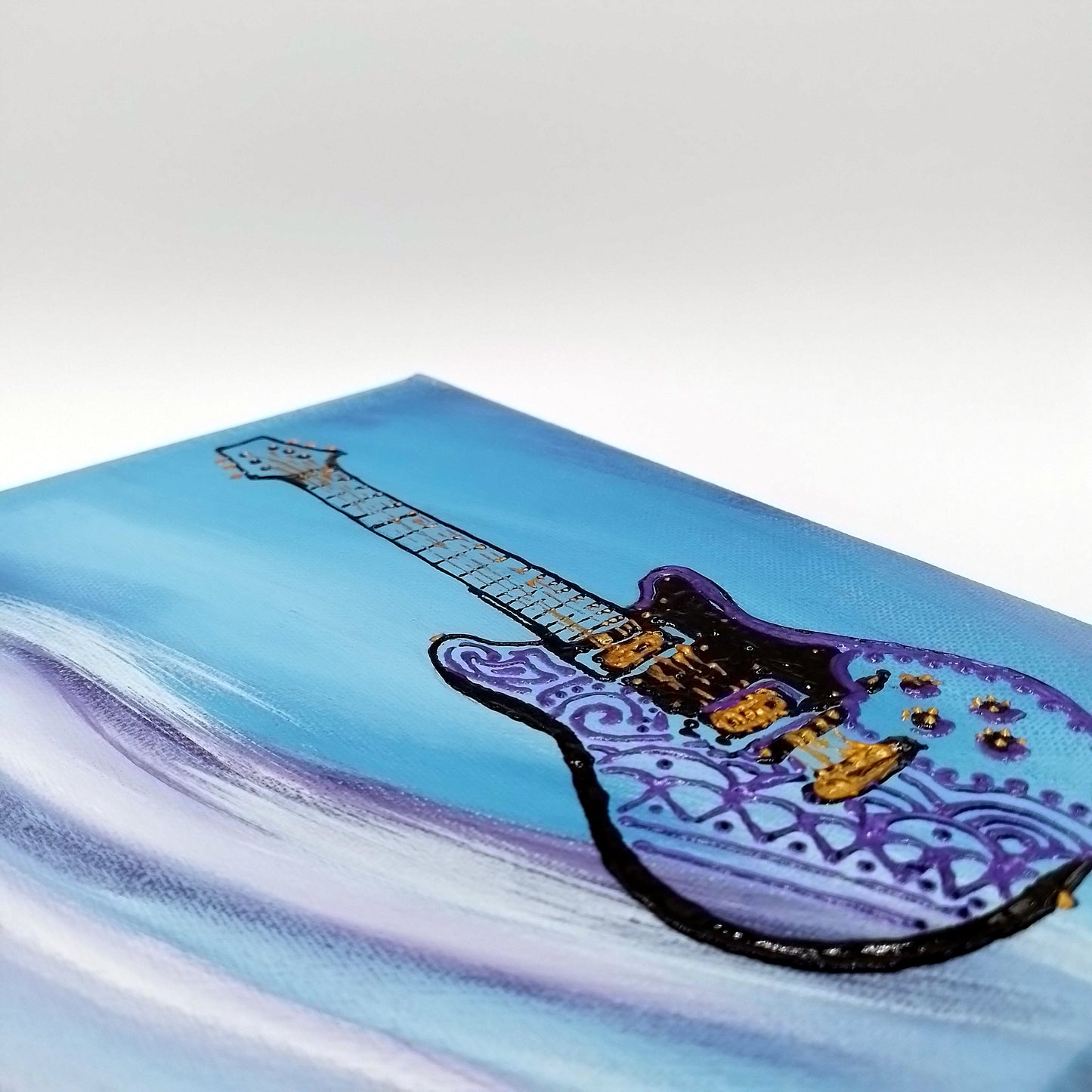Detail of the painting with black and purple electric guitar on blue white and purple background. The shape of the instrument is a light relief on a flat surface.