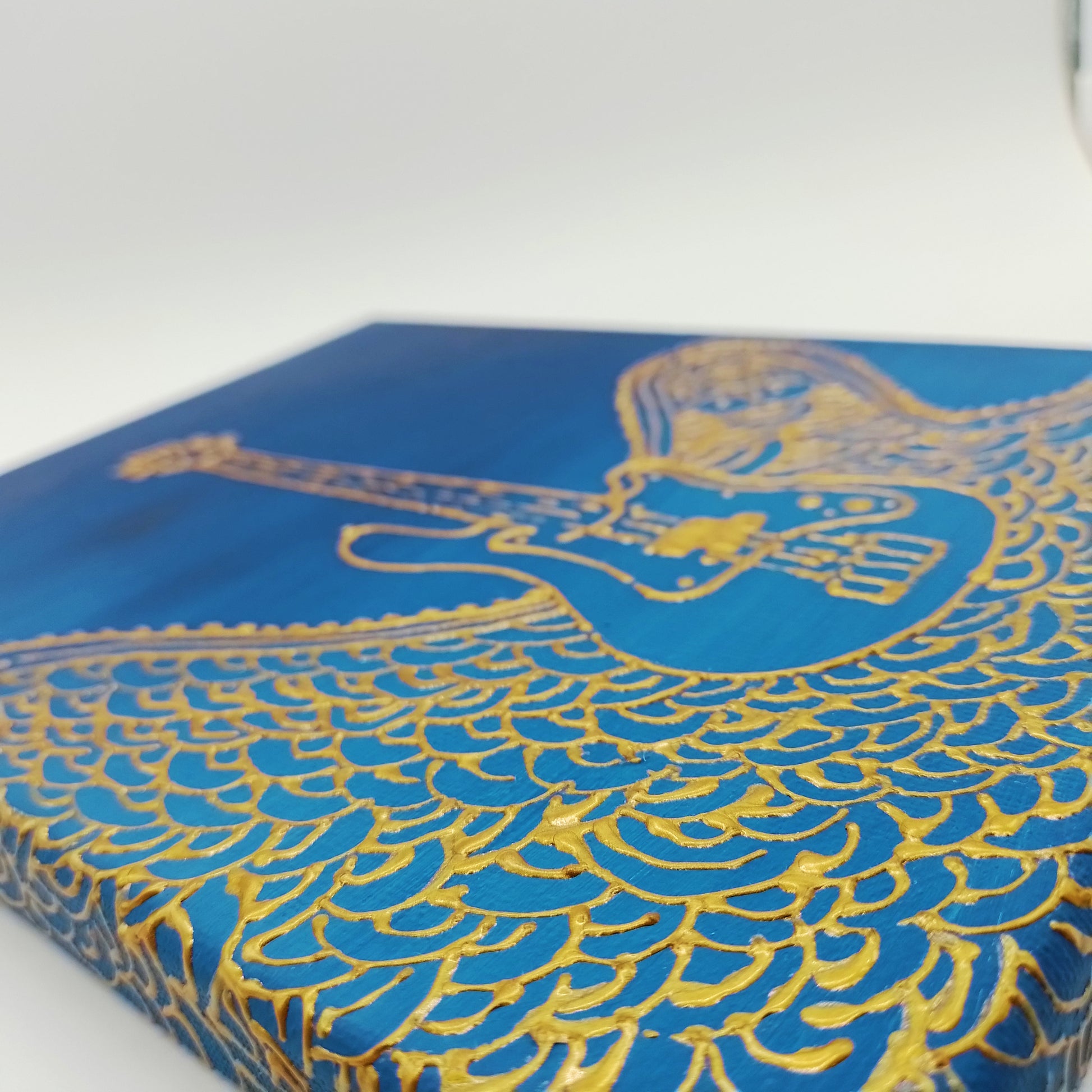 Detail of the painting with gold electric bass guitar and decorative elements on blue  background. The shape of the instrument is a light relief on a flat surface.