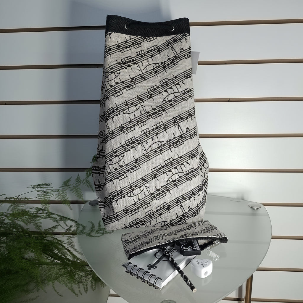 A drawstring bag with a black and white musical staff pattern, displayed on a glass table with a matching pouch, notebook, and pen.
