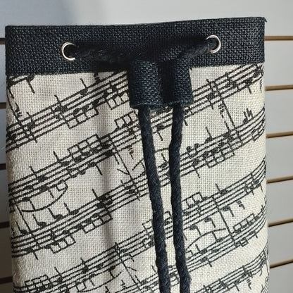 A fabric drawstring bag featuring a black and white musical staff pattern, with a black woven top band and matching black drawstring cords.