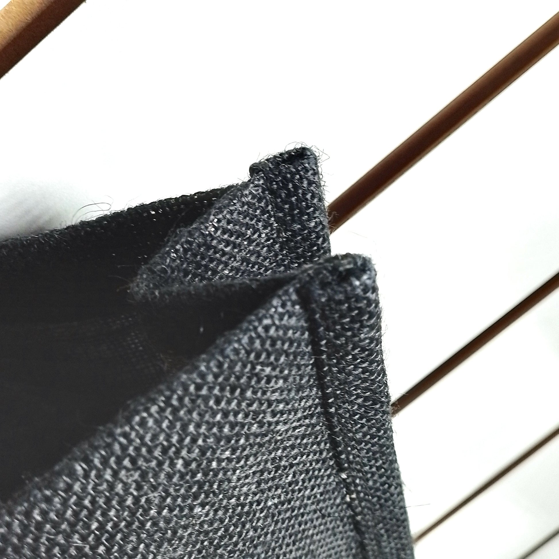 Close-up of a dark charcoal grey woven fabric, showing the texture and folded edges against a bright white background.