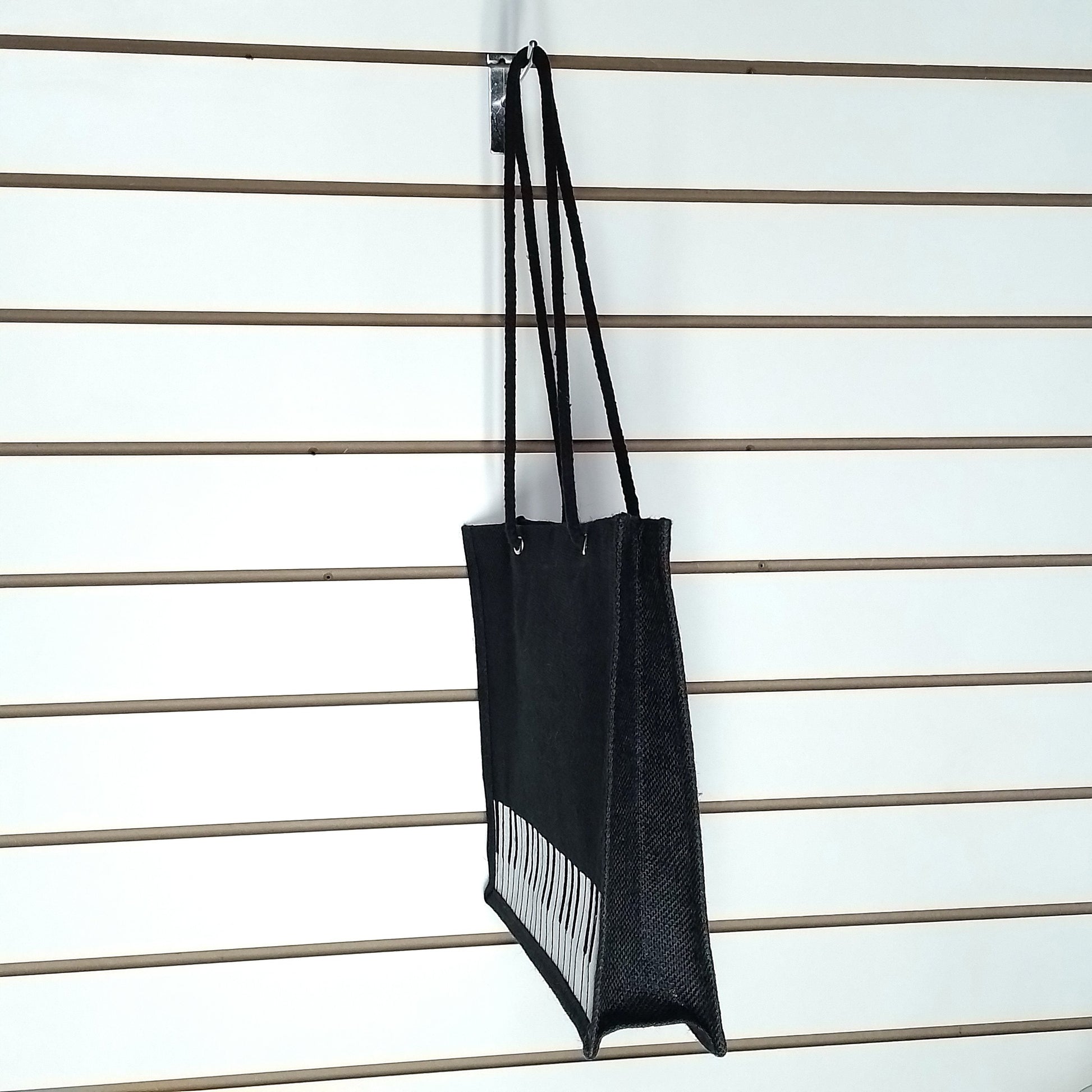 A sideview of a black Music Themed Reusable Shopping Bag, displayed on a white slatted wall.