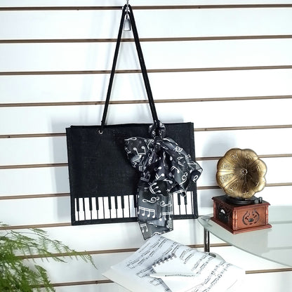 A black Music Themed Reusable Shopping Bag, styled with a black and white music note print scarf, displayed on a white slatted wall alongside sheet music, a small wooden box, and a gold gramophone ornament.