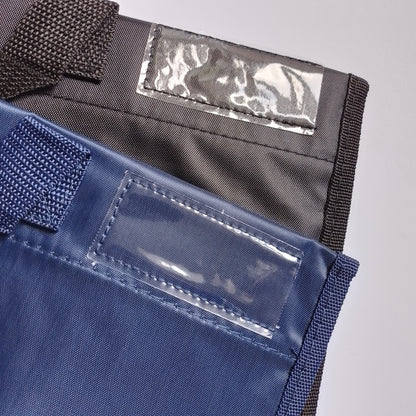 Close-up of two fabric pouches or sleeves with clear plastic ID windows and dark woven straps, shown on a light gray background.