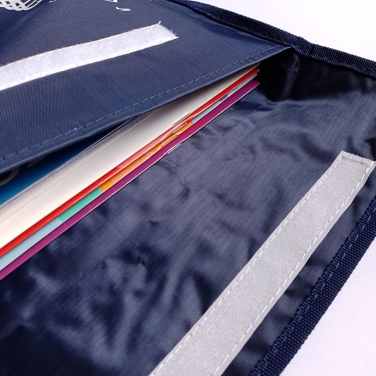 Close-up of a navy blue fabric music bag with a flap, showing a stack of colourful paper or card inserts and a reflective light grey strip on the inside.