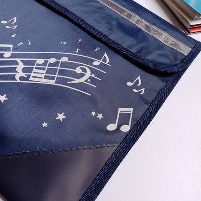 A navy blue fabric music bag with white musical notes, staff lines, and stars printed on it, shown on a white surface with part of a book visible in the top right corner.