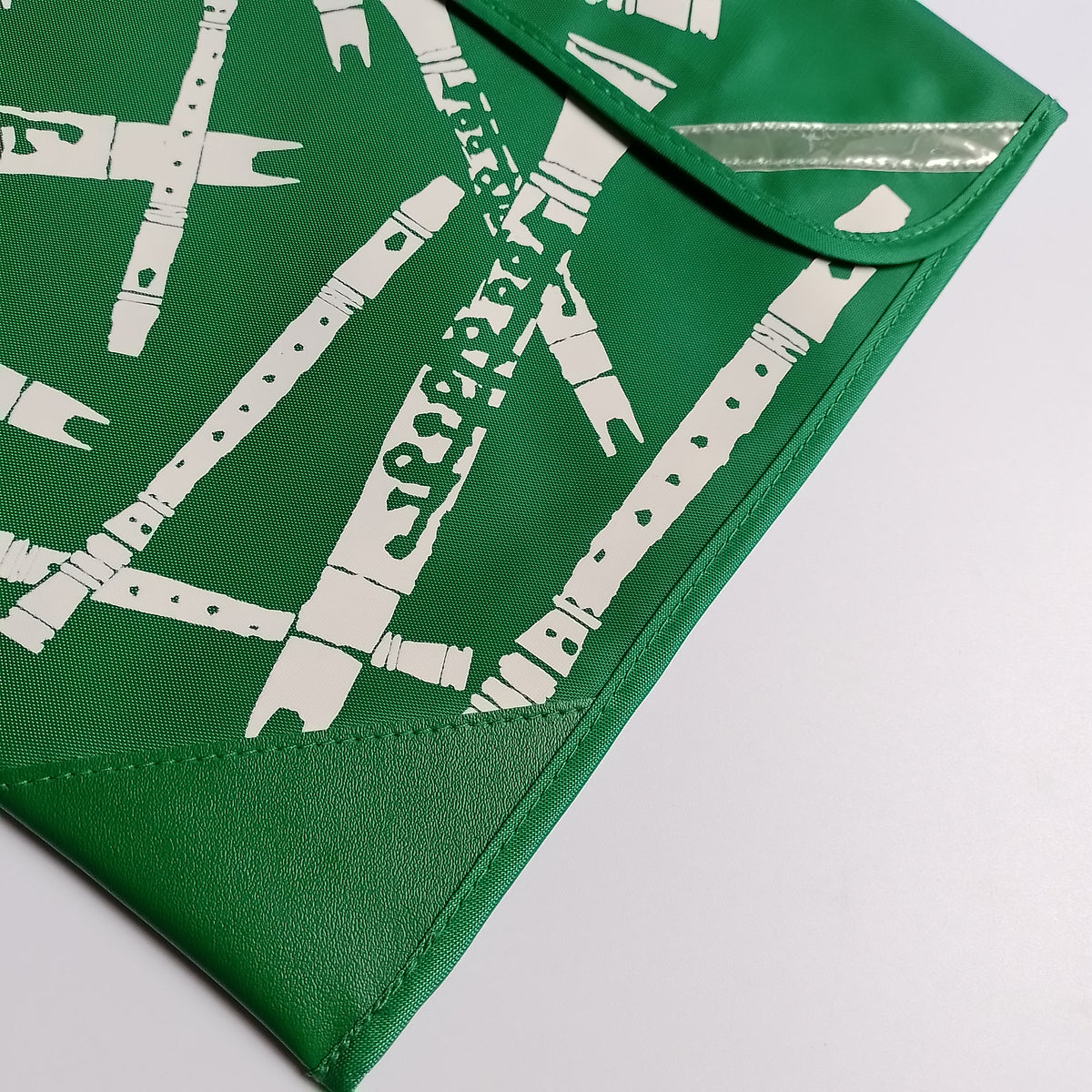 A close-up of a green envelope-style pouch or clutch with a white bamboo graphic print and a reflective silver strip on the flap, photographed on a light gray background.