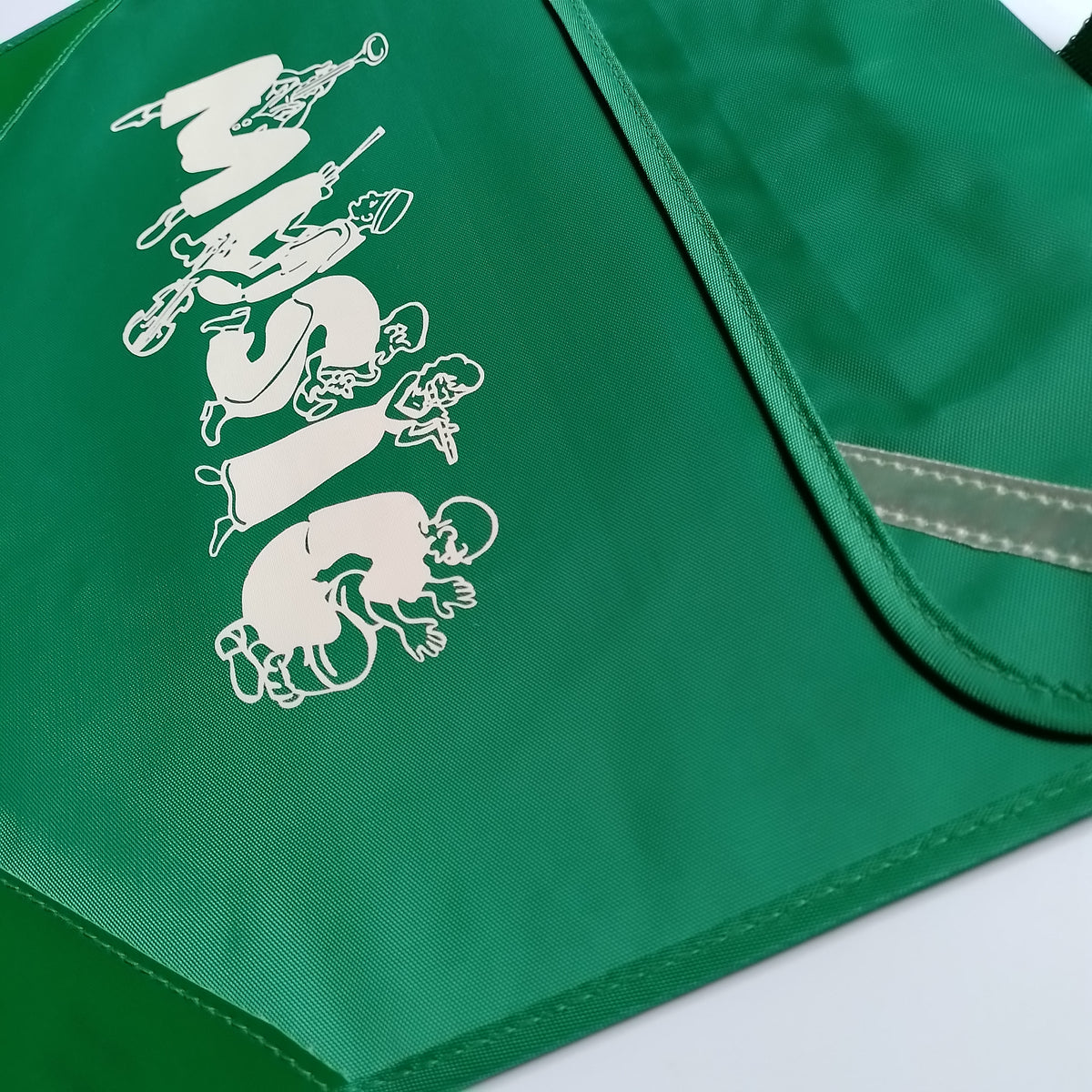 A close-up of a green fabric item, likely a bag or pouch, featuring a white graphic print of cartoon figures spelling 'MUSIC' and a reflective silver-gray strap.