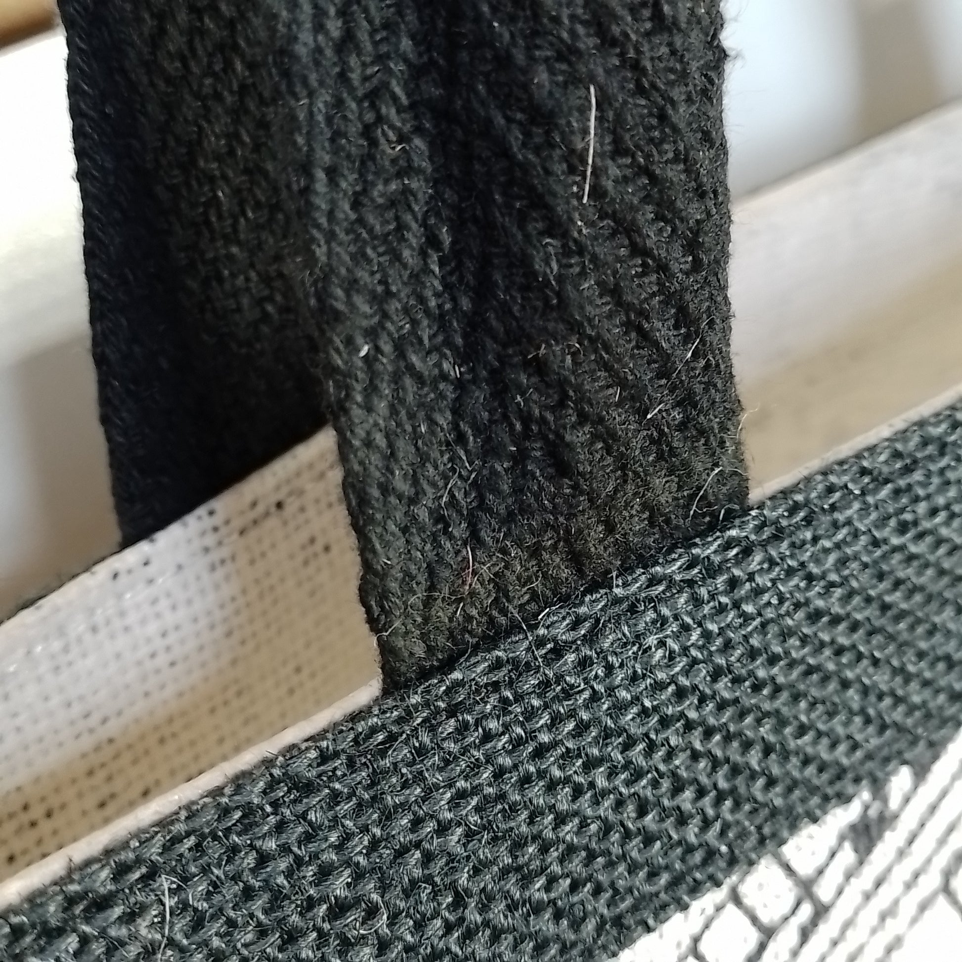 Close-up of a black woven fabric strap or handle attached to a white mesh bag, showing the texture of the material.