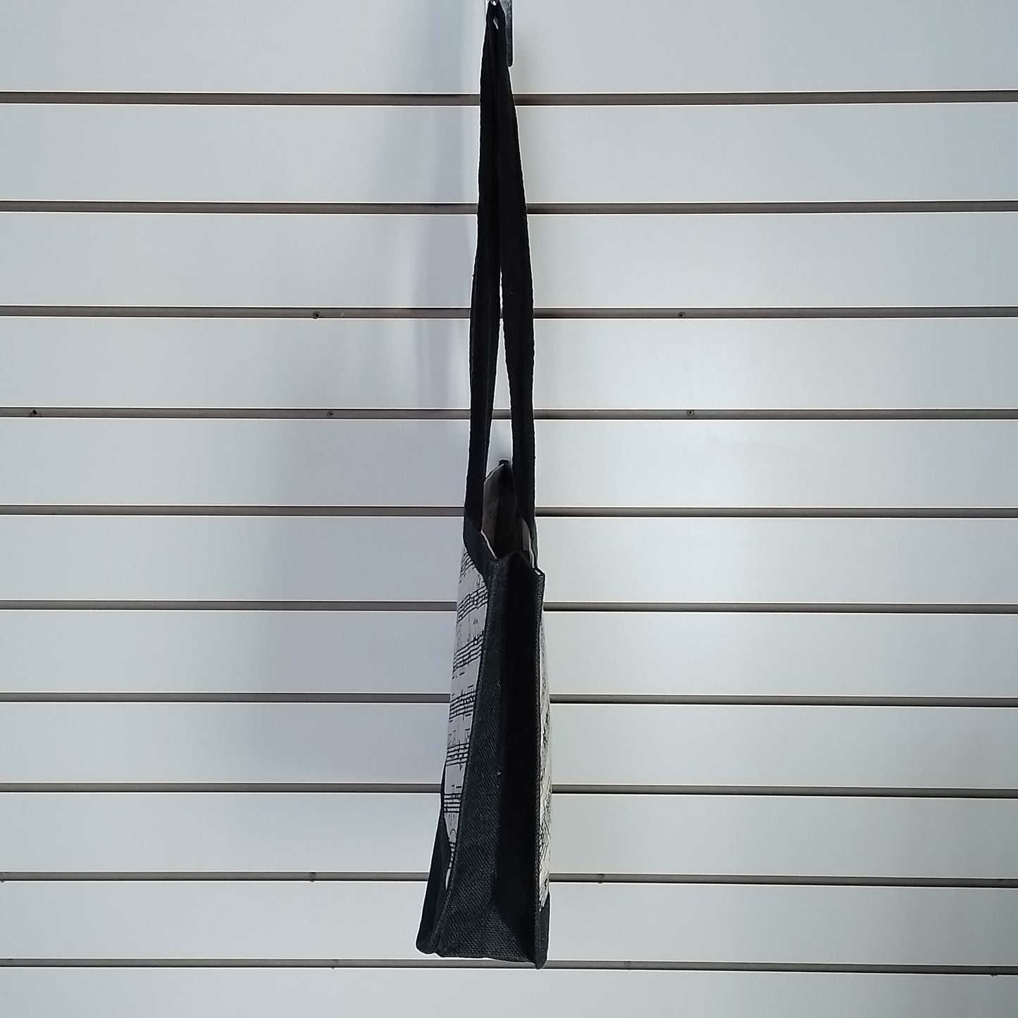 A black and white patterned tote bag hanging from a hook on a white slatwall display.