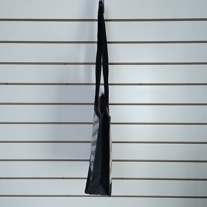 A black and white patterned tote bag hanging from a hook on a white slatwall display.