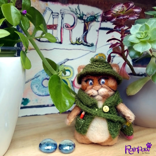 Small ginger cat/ tiger figurine in a green outfit, a pencil sticking out of its pocket  and messenger bag with plants and a colourful background