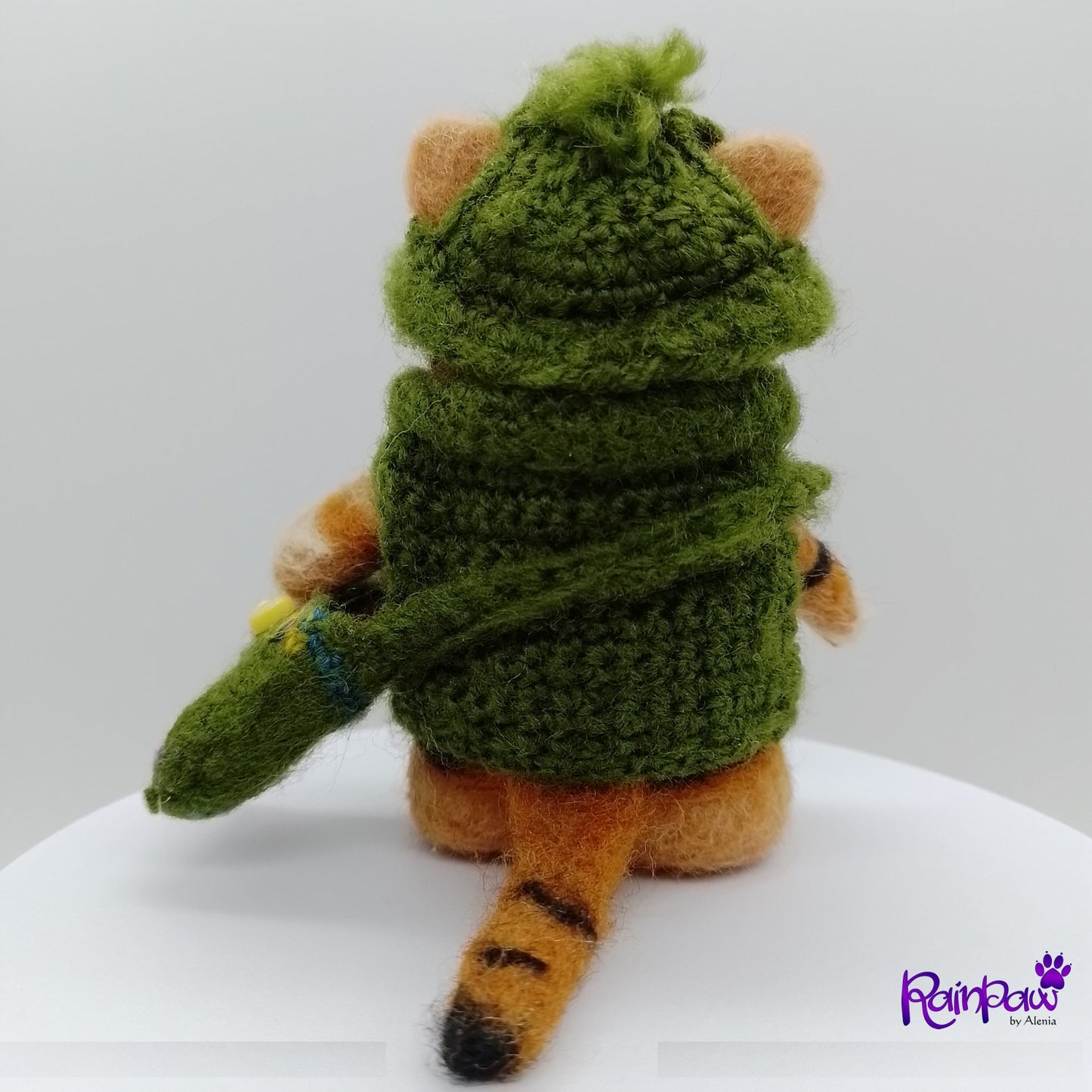 Small plush with a green hood and orange, black and brown body on a white surface