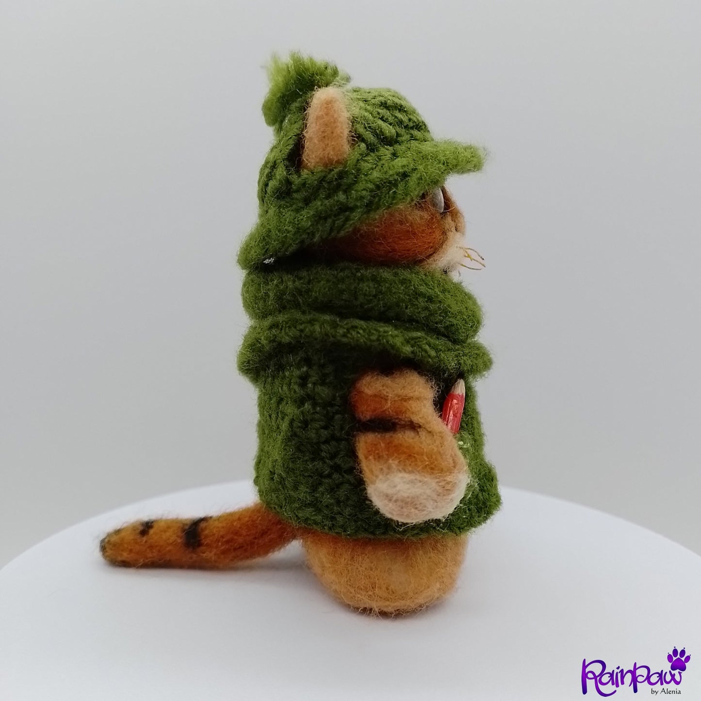 Plush ginger cat/tiger in a green sweater on a white surface with a light grey background