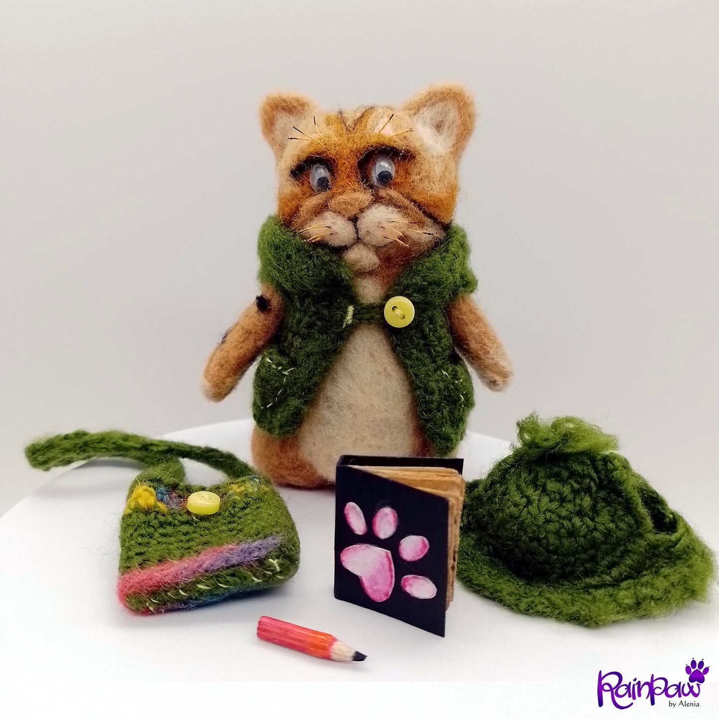 Cat-shaped plush toy with green hat, small bag, and book on a white background