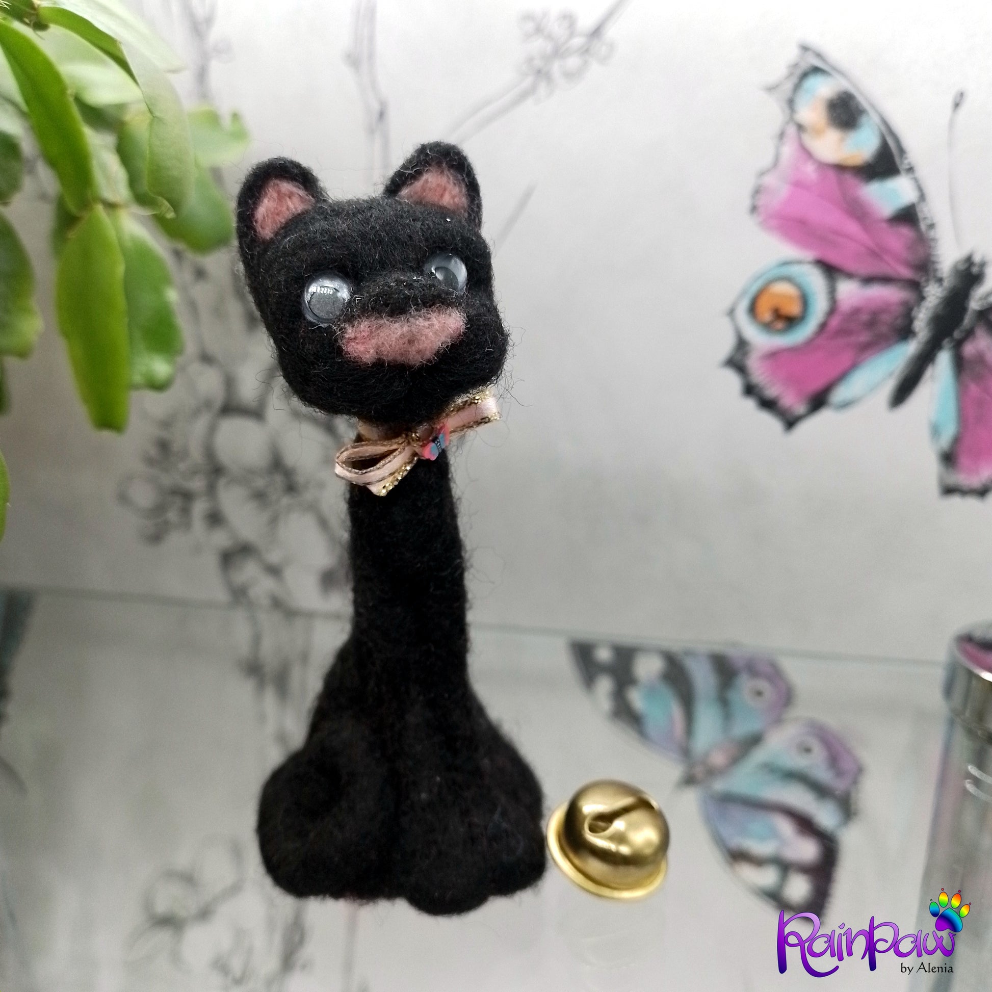 Black cat-shaped figurine with a gold bell on a decorative background with butterfly stickers.