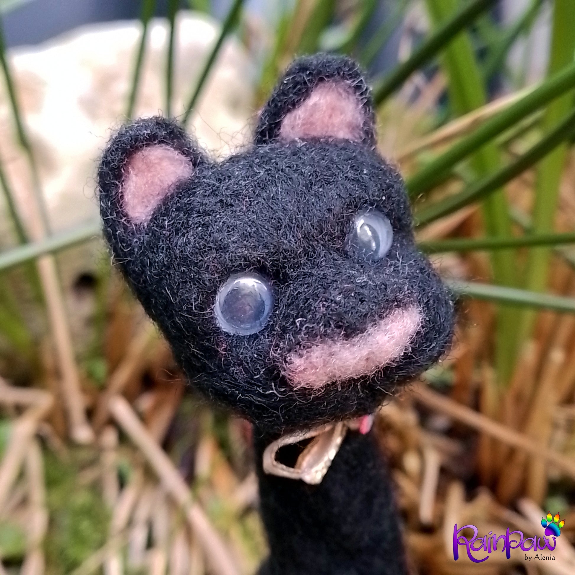 Black cat-shaped plush with pink inner ears and nose against a natural background