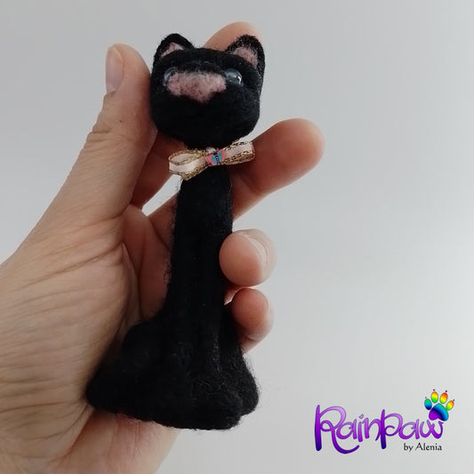 Black cat-shaped figurine with a bow held in a hand against a white background, featuring the brand 'Rainpaw'.