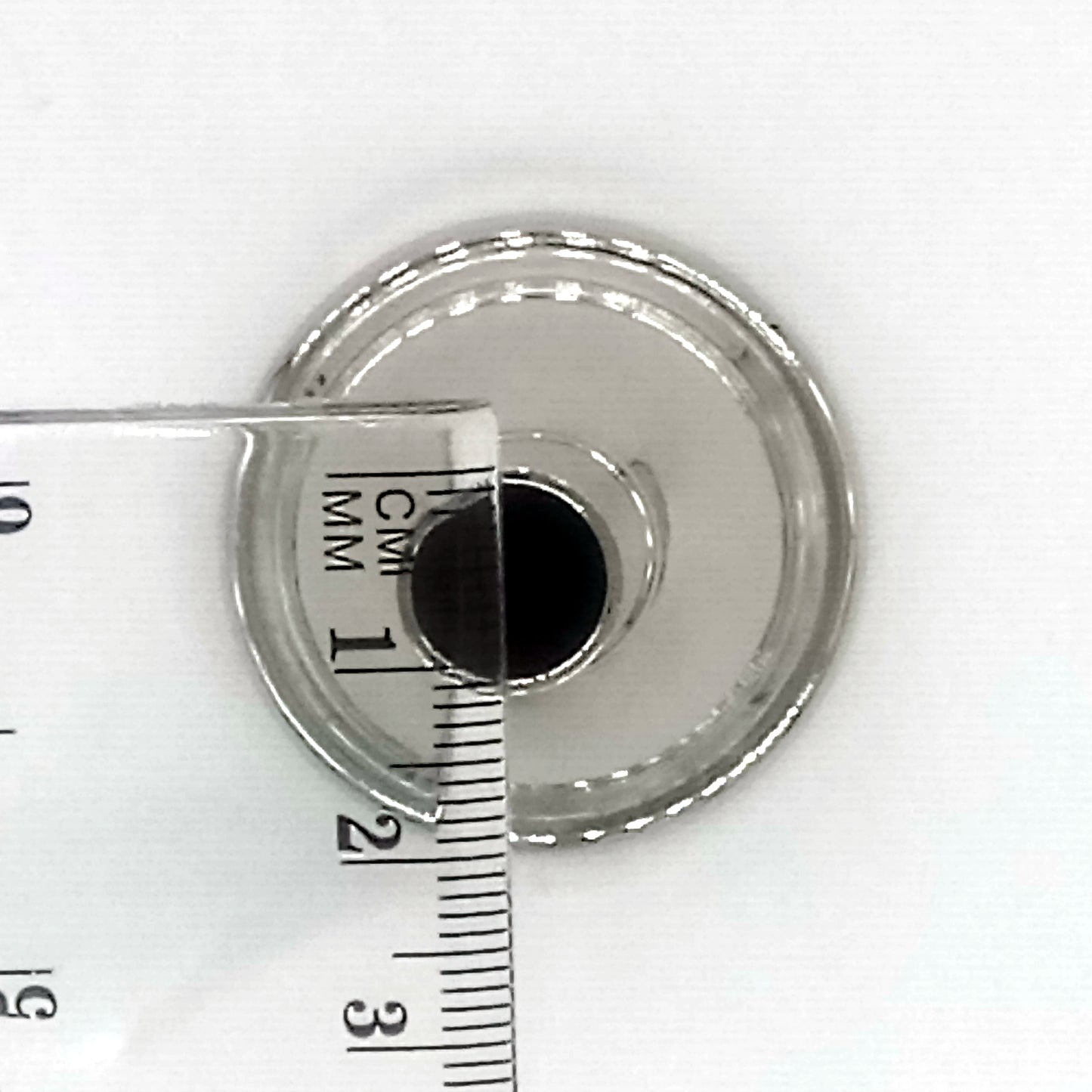 A view of the metallic circular side that attaches to the instrument with a ruler which indicates 1 cm 