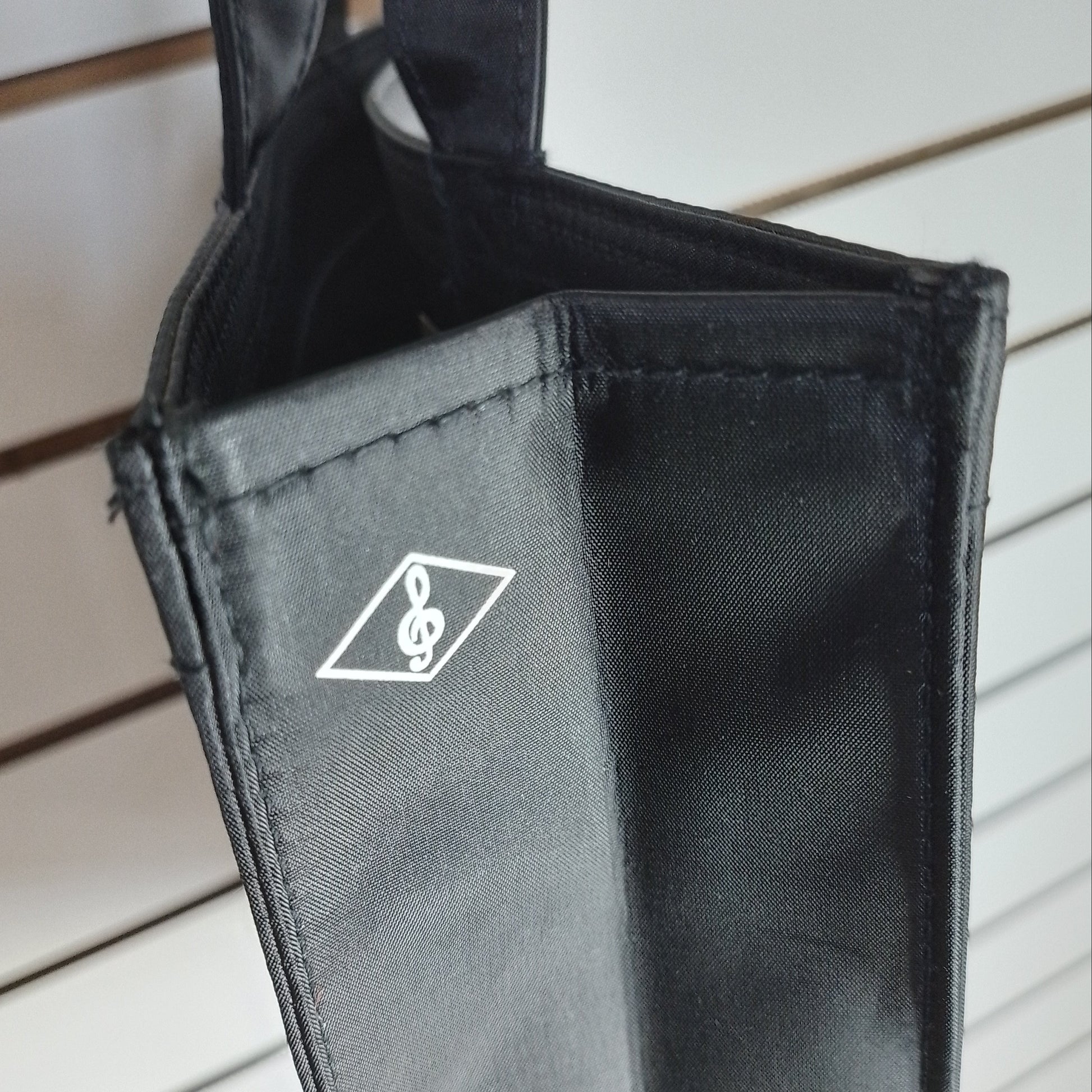 A close-up of a black fabric accessory, likely a bag or sleeve, featuring a white printed logo of a treble clef inside a diamond shape, set against a light-coloured slatted background.