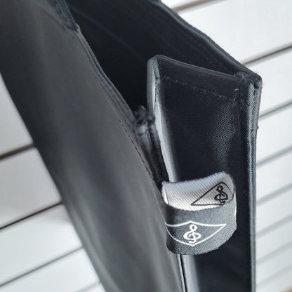 Close-up of a black fabric accessory with a small gray fabric tag featuring a white stylized logo, shown against a white slatted wall background.