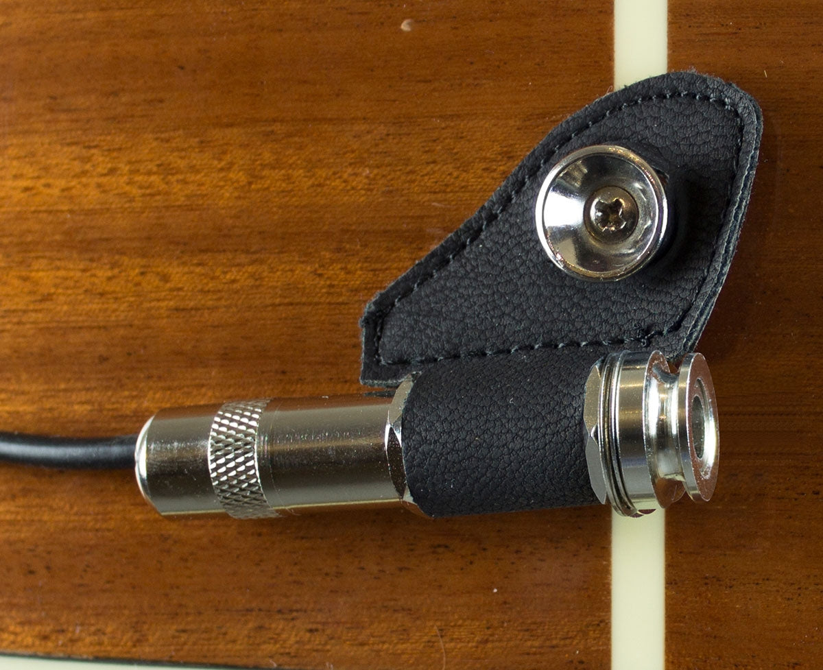 Close-up of a guitar pickup output on a wooden guitar body in a leather harness that nests the Jack near a strap button