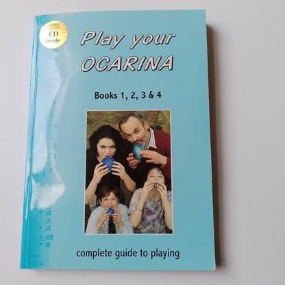 A book titled 'Play your OCARINA' for Books 1, 2, 3 & 4, featuring a light blue cover with a photo of a family playing with blue ocarina. A gold 'INCLUDES CD' sticker is visible in the top-left corner.