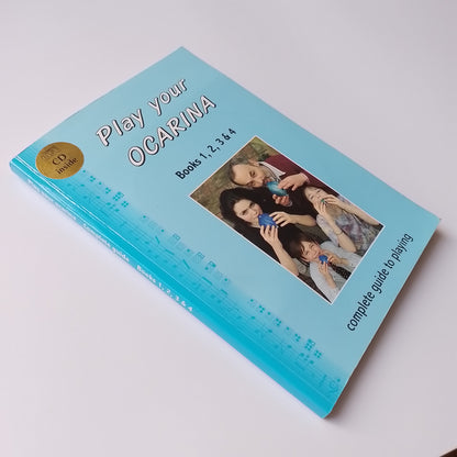A book titled 'Play your OCARINA' for Books 1, 2, 3 & 4, featuring a light blue cover with a photo of a family playing with blue ocarina. A gold 'INCLUDES CD' sticker is visible in the top-left corner.