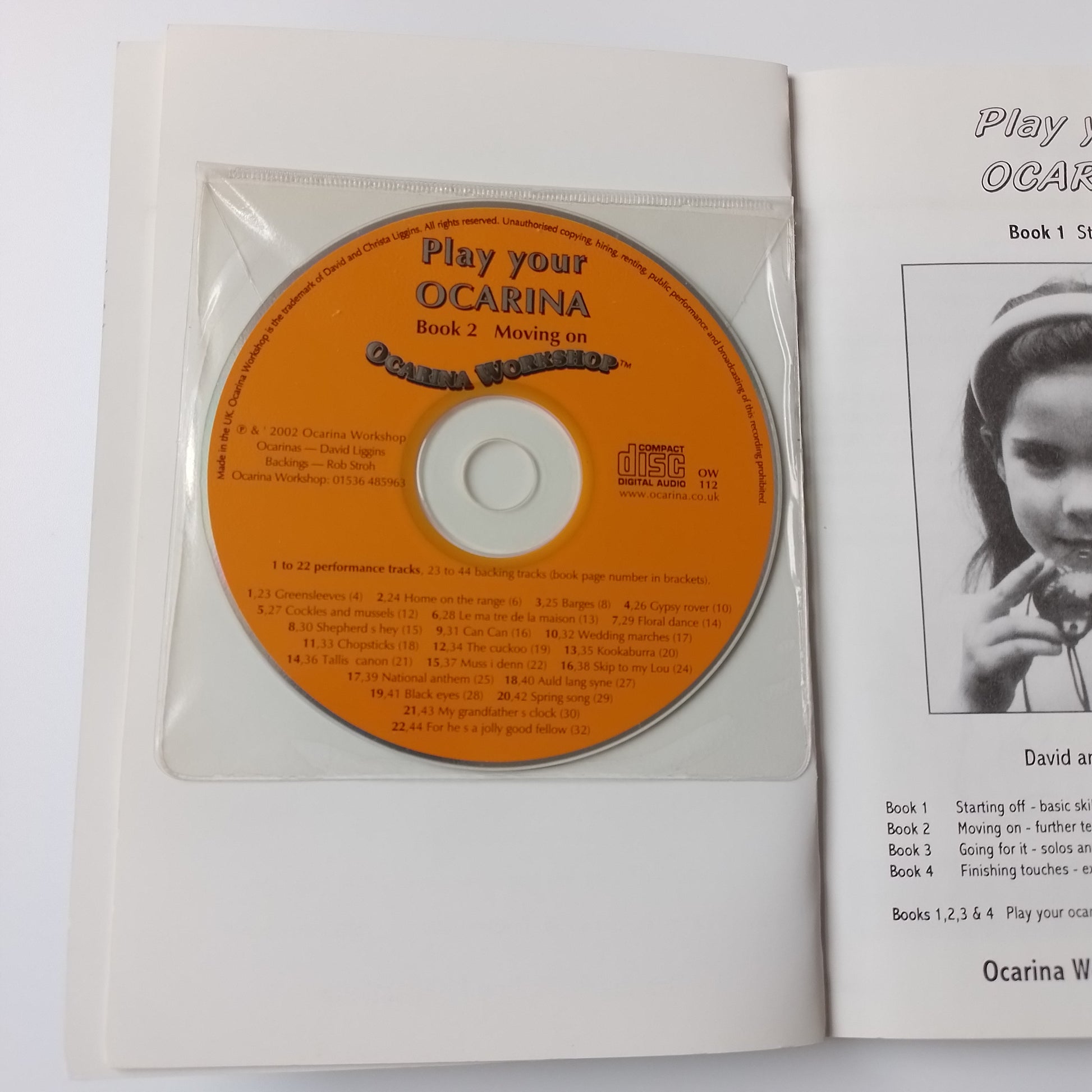 An open book or booklet showing a CD inside a clear plastic sleeve. The CD has an orange label with the title 'Play your OCARINA' and track listing text.