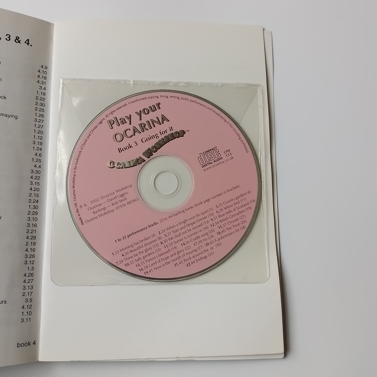 A pink compact disc with printed text, displayed inside an open white booklet or case on a plain light background.