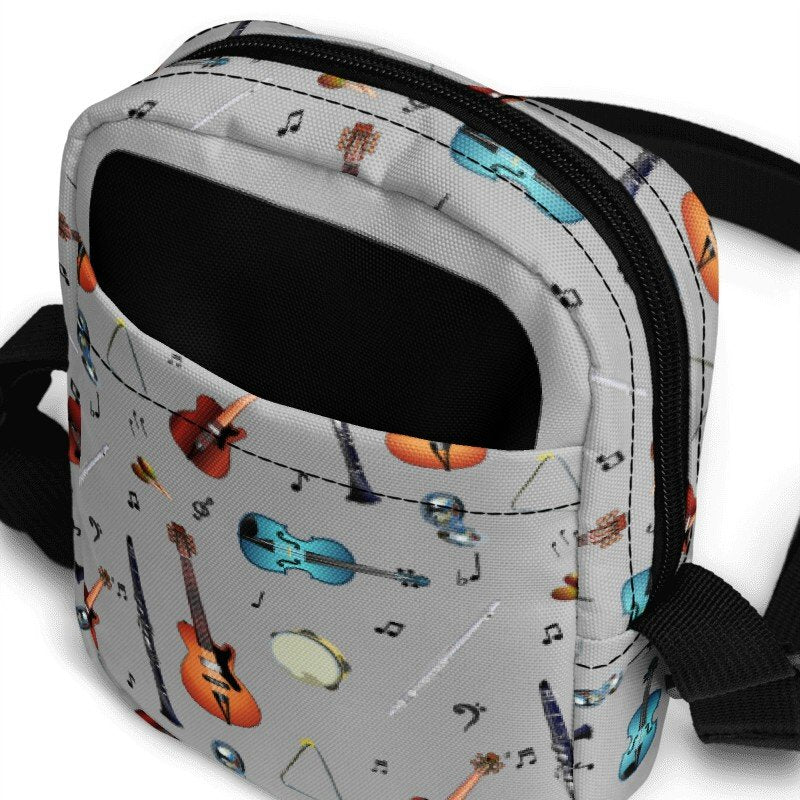 Grey crossbody bag with black adjustable shoulder strap (with black plastic clip), inside and outside pockets, sturdy fabric, and two-way zipper. The design features a repeat pattern of colourful musical instruments and black musical notes on a grey background.